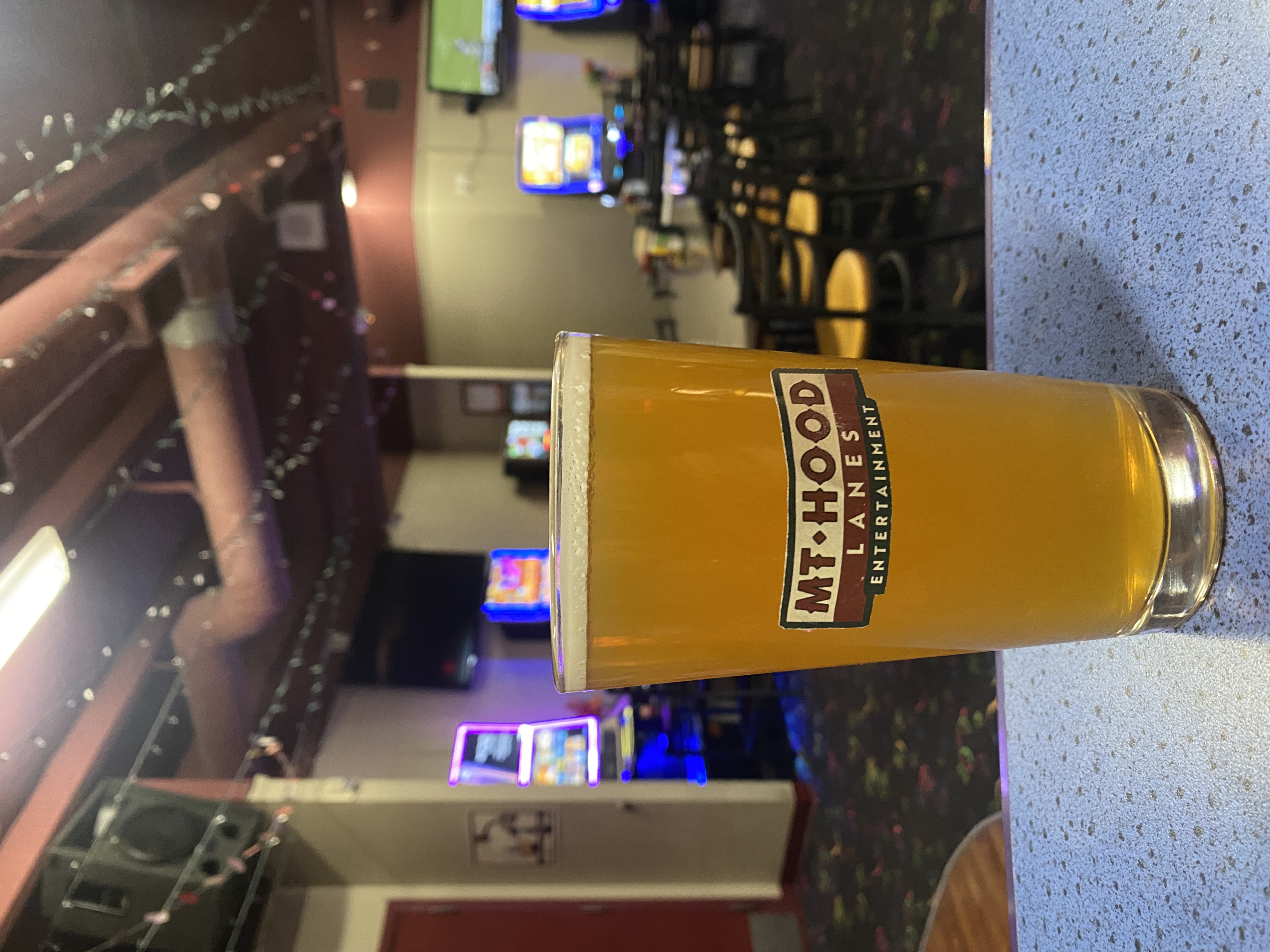 Pint glass of beer with a mt hood lanes logo, with a view of the lava lounge